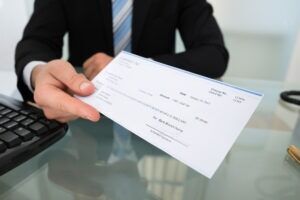 A man holds a check in his hands as he repays workers' compensation benefits. Consult with an attorney to learn why you would have to pay back workers' compensation.