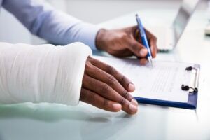 A worker with an injured arm filling out paperwork. Find out what types of injuries are covered by workers’ compensation today.