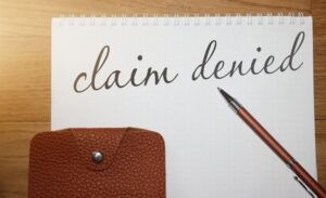 The words "denied claim" appear on a notepad. You can consult an attorney to learn how to prove a bad faith claim against an insurance company.