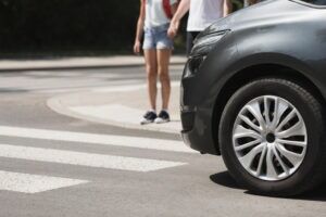 Pedestrians wait for a car to stop at an intersection so they can walk across the street as they wonder what the average settlement for a pedestrian hit by a car is.