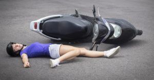 young woman lying on pavement with her leg bent back after a motorcycle accident