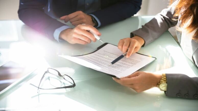 Two Lawyers Hand Analyzing Document Over Glass Desk