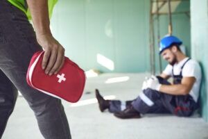 A coworker brings a first aid kit to help an injured worker. They discuss the benefits of hiring a workplace injury lawyer in Burlington.