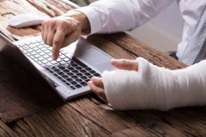 An injured man using a laptop wonders who qualifies for workers’ compensation
