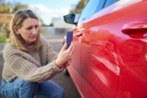 A woman examines the damage to her car after an accident. Car insurance typically covers the vehicle, not the driver, but exceptions exist depending on the policy and situation. Consult a car accident attorney about your options for recovering damages.