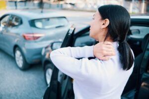 A woman stands in front of a fender bender holding her neck, wondering whether a fender bender counts as an accident.