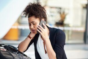 A frustrated woman talking on the phone while looking at her car. Learn about who pays the deductible in a car accident.